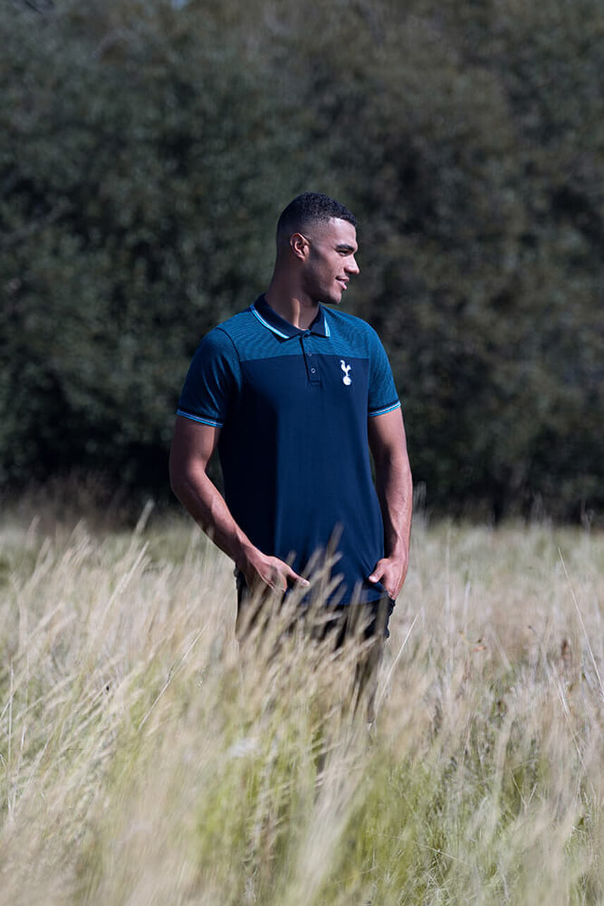 A male model standing in a field wearing a blue tottenham hotspur polo shirt