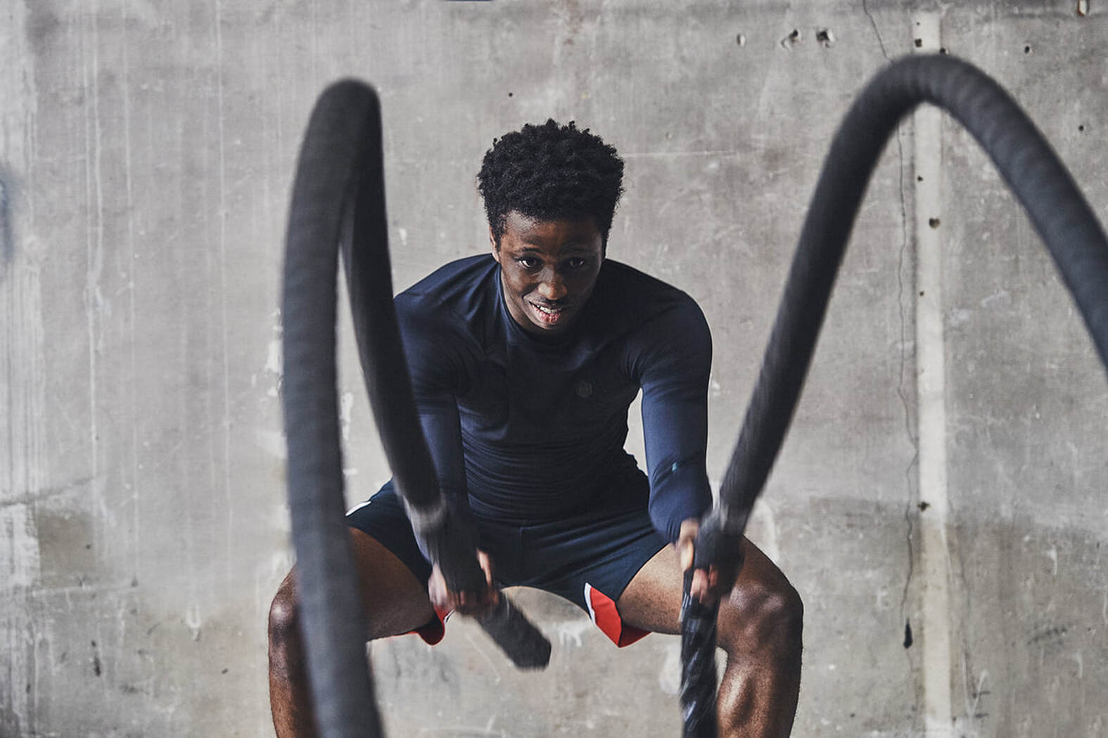 football player excersising with battle ropes wearing a black under armour training top and southampton fc shorts
