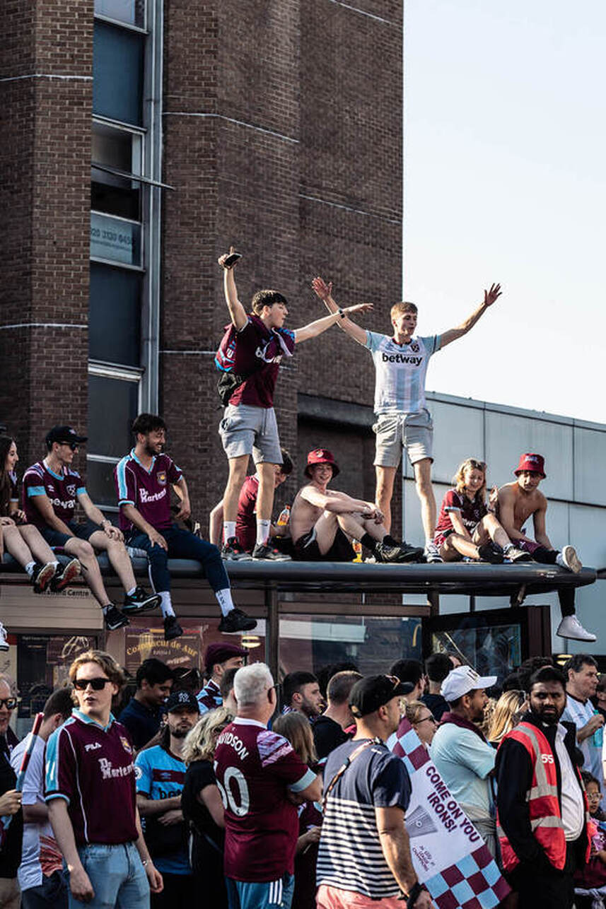 west ham fans on top of a bus stop celebrating winning the europa cup