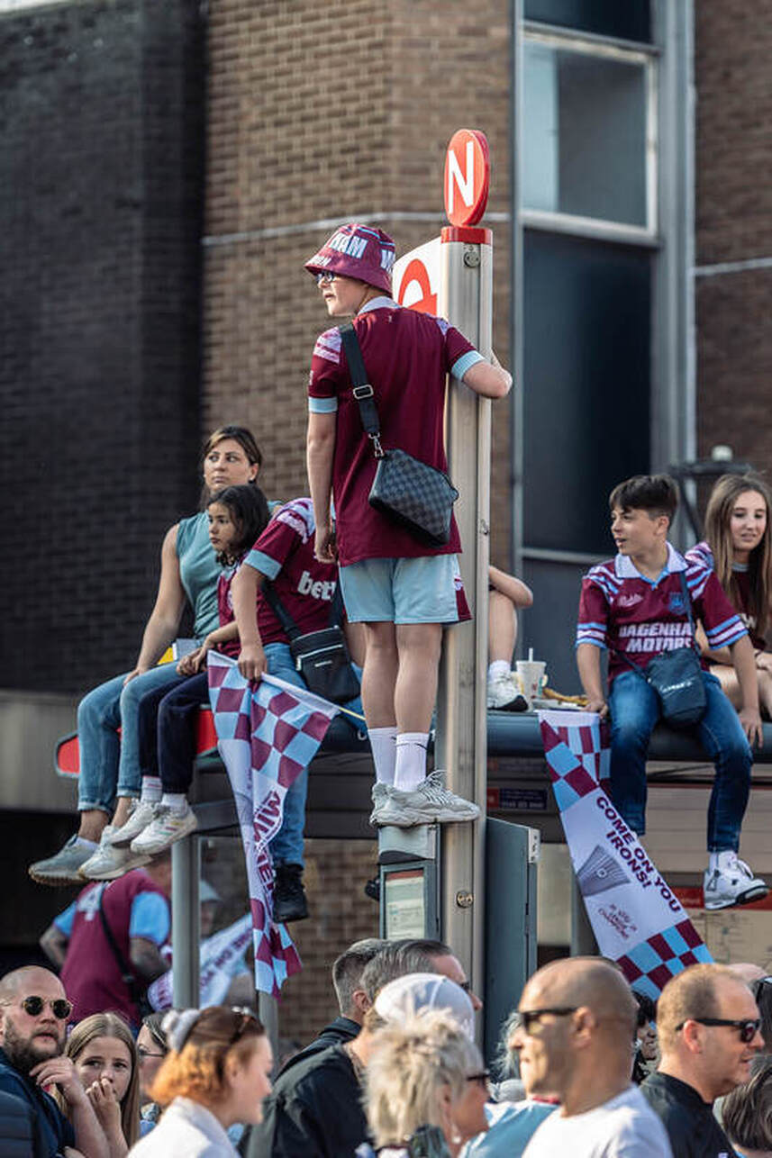west ham fans on top of a bus stop celebrating winning the europa cup