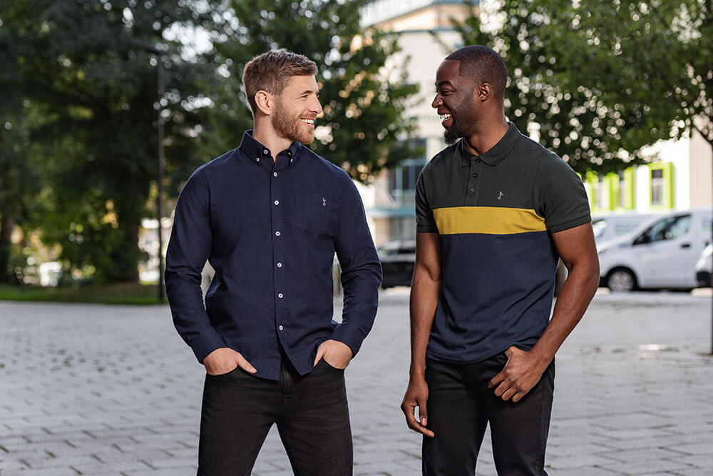 two male models standing in a city one is wearing a blue tottenham hotspur shirt and the other wearing a green, yellow and blue polo shirt