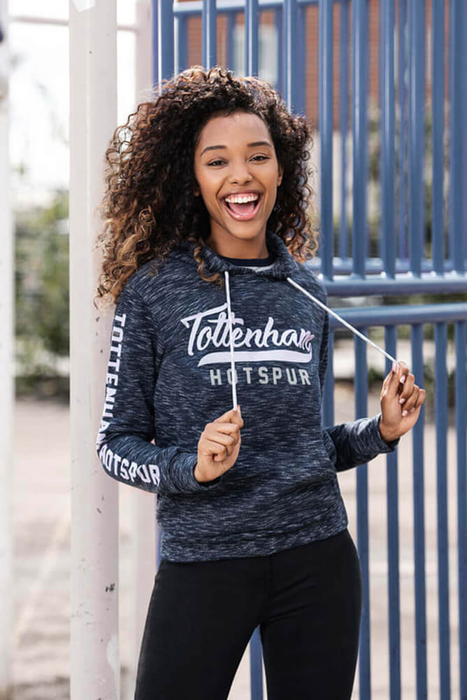 A female model standing in a playground wearing a blue tottenham hotspur hoody