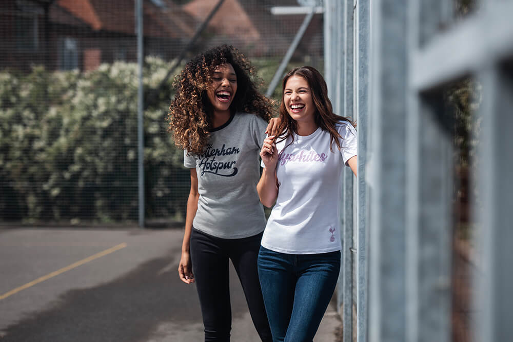 two female models laughing in an outdoor basketball court, wearing tottenham hotspur tee shirts