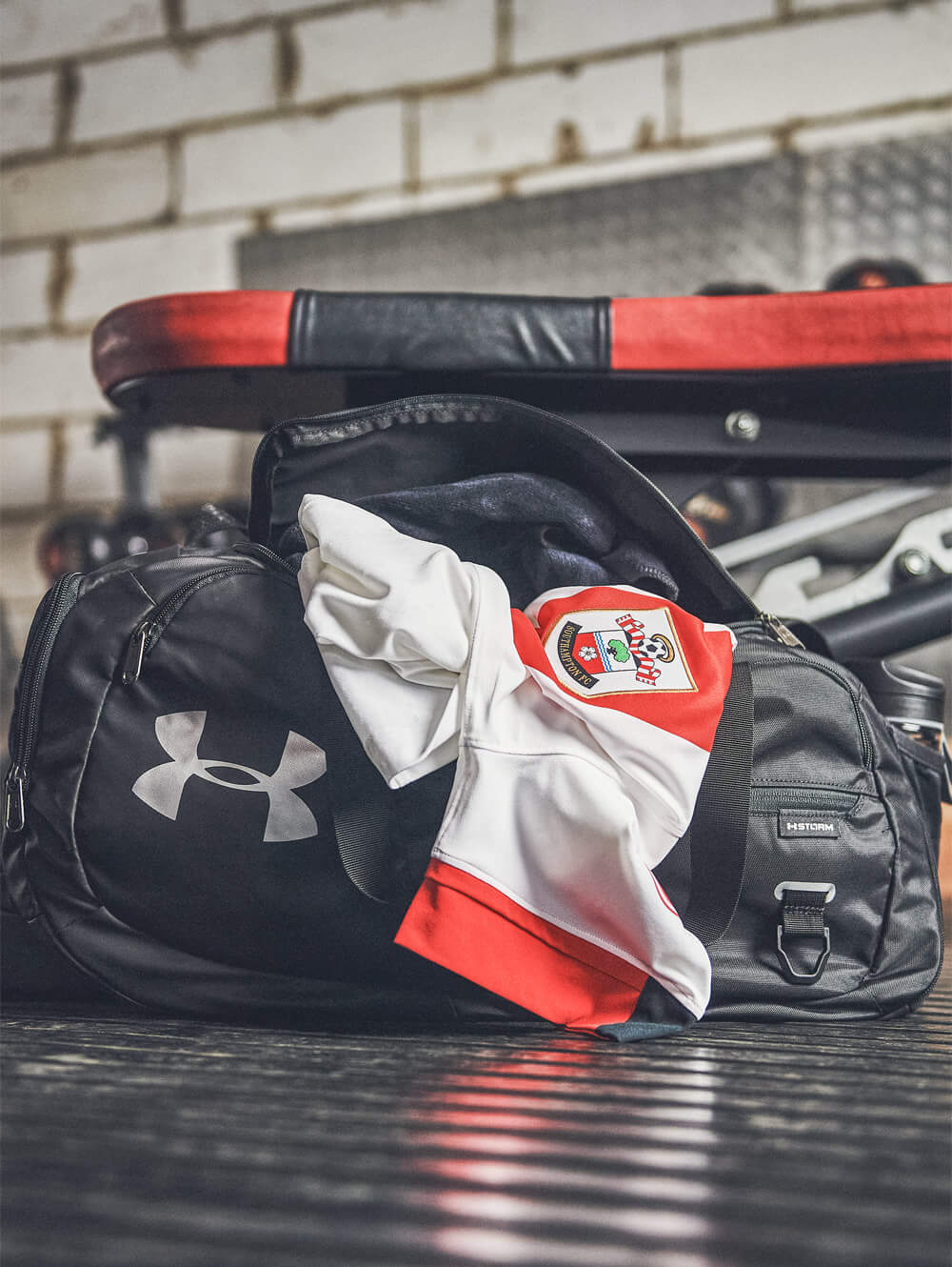 white and red southampton fc football shirt poking out of a black under armour sports bag