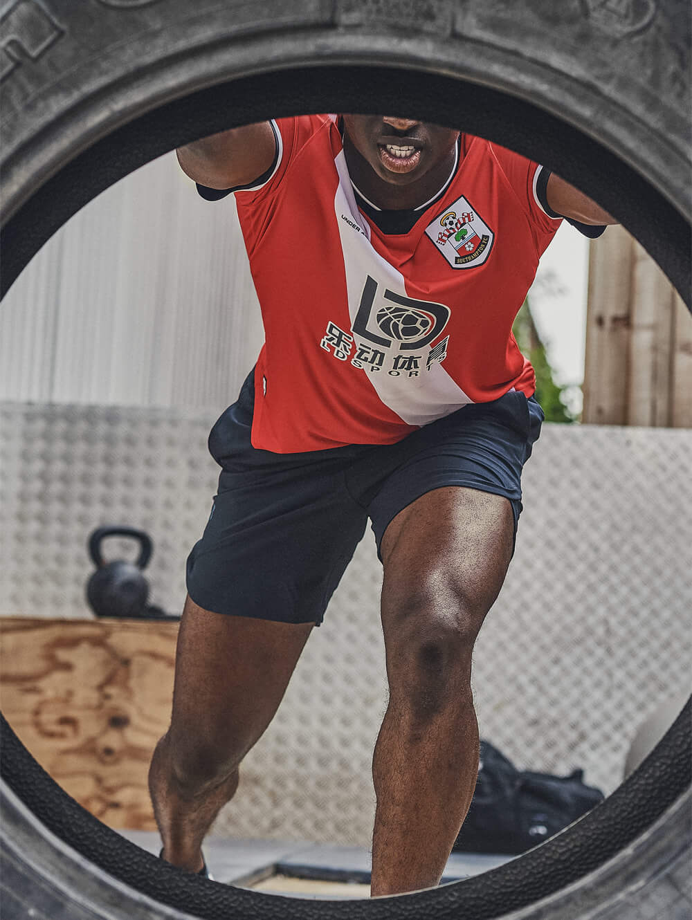 football player excersising with a tractor tyre, wearing a red and white southampton fc shirt